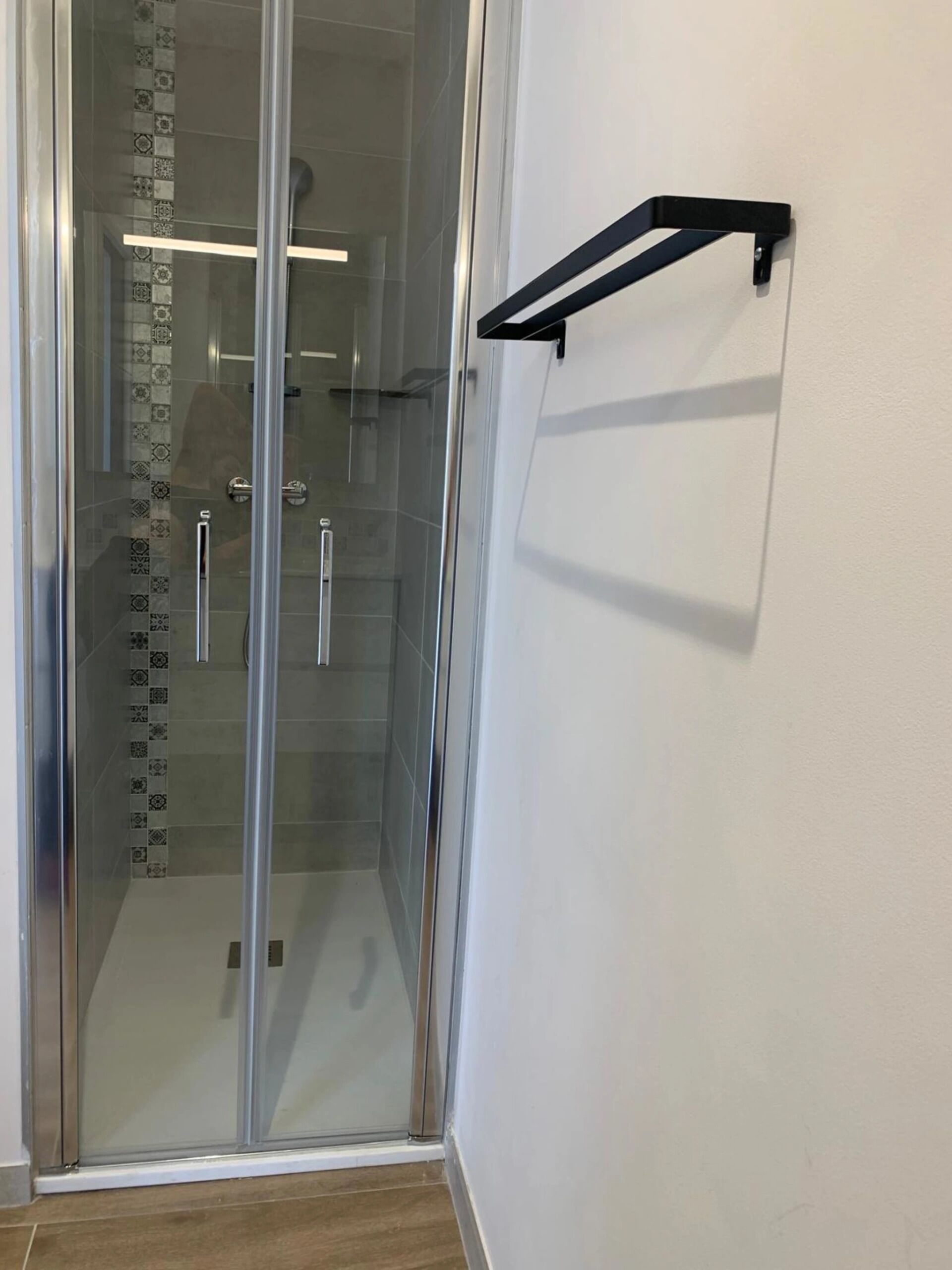 A glass-enclosed shower with a black towel rack on the wall.