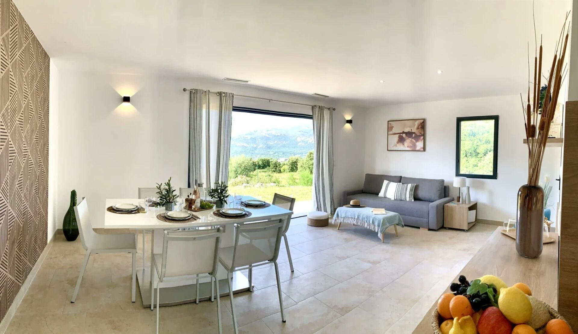 A modern living room with a dining area, large windows, and a view of the outdoors.