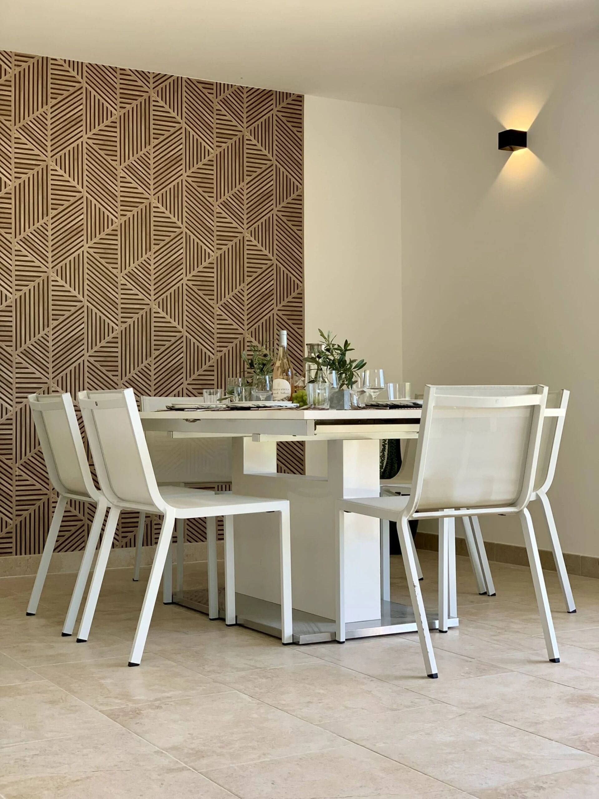 Ein moderner Essbereich mit einer Wand im geometrischen Muster, einem zentralen Tisch mit Stühlen und einer wandmontierten Leuchte.