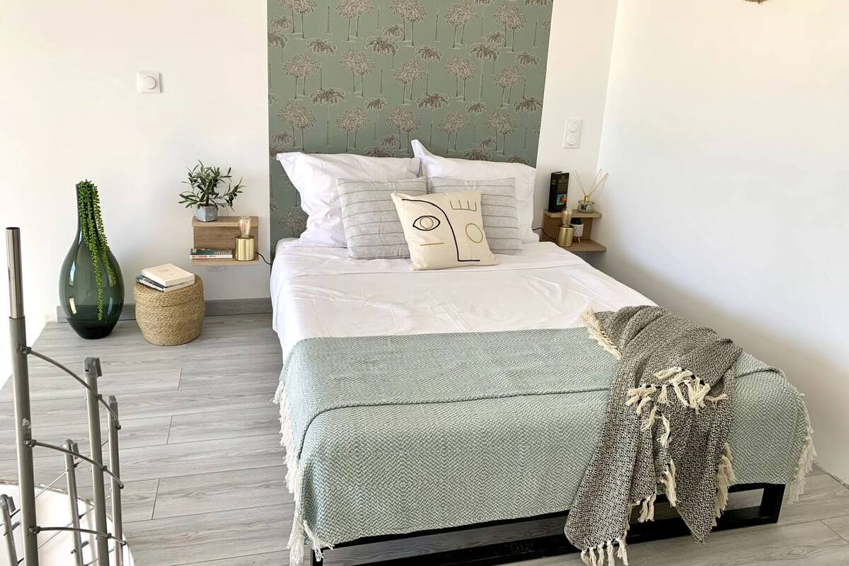 A neatly arranged bedroom with a bed, bedside tables, a wall clock, a small plant, and a decorative wall piece.