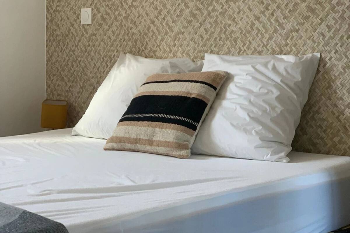 A hotel room with a bed, a headboard with a woven pattern, and three framed artworks on the wall.