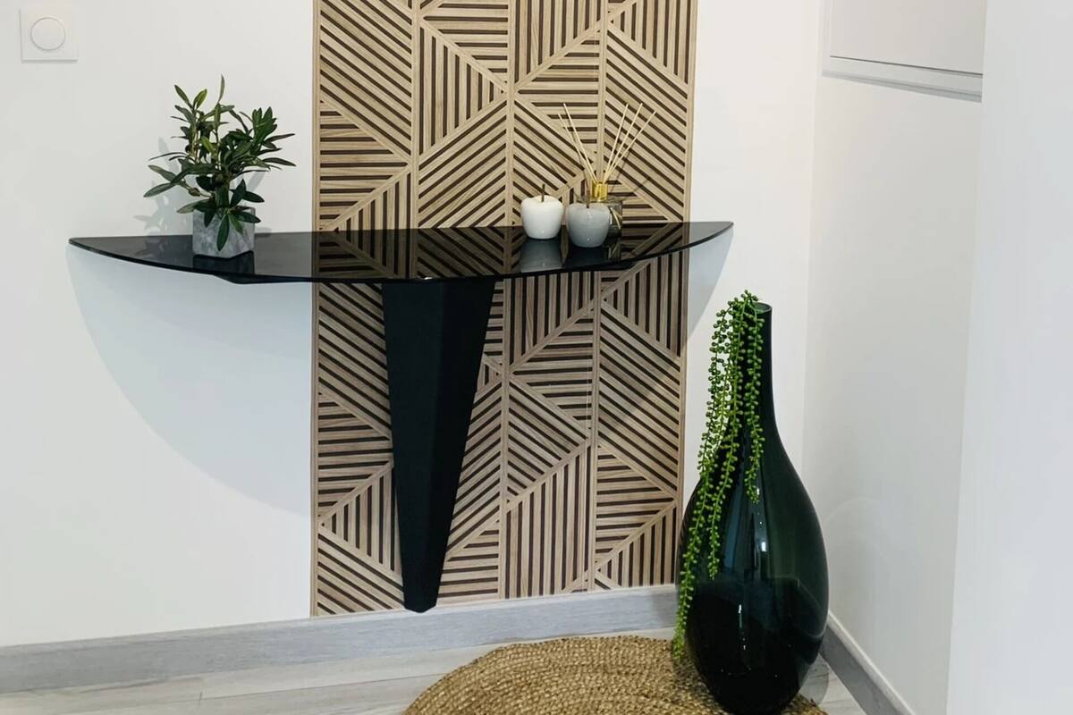 A modern interior with a geometric patterned wall, a glass console table with decorative items, and a potted plant.