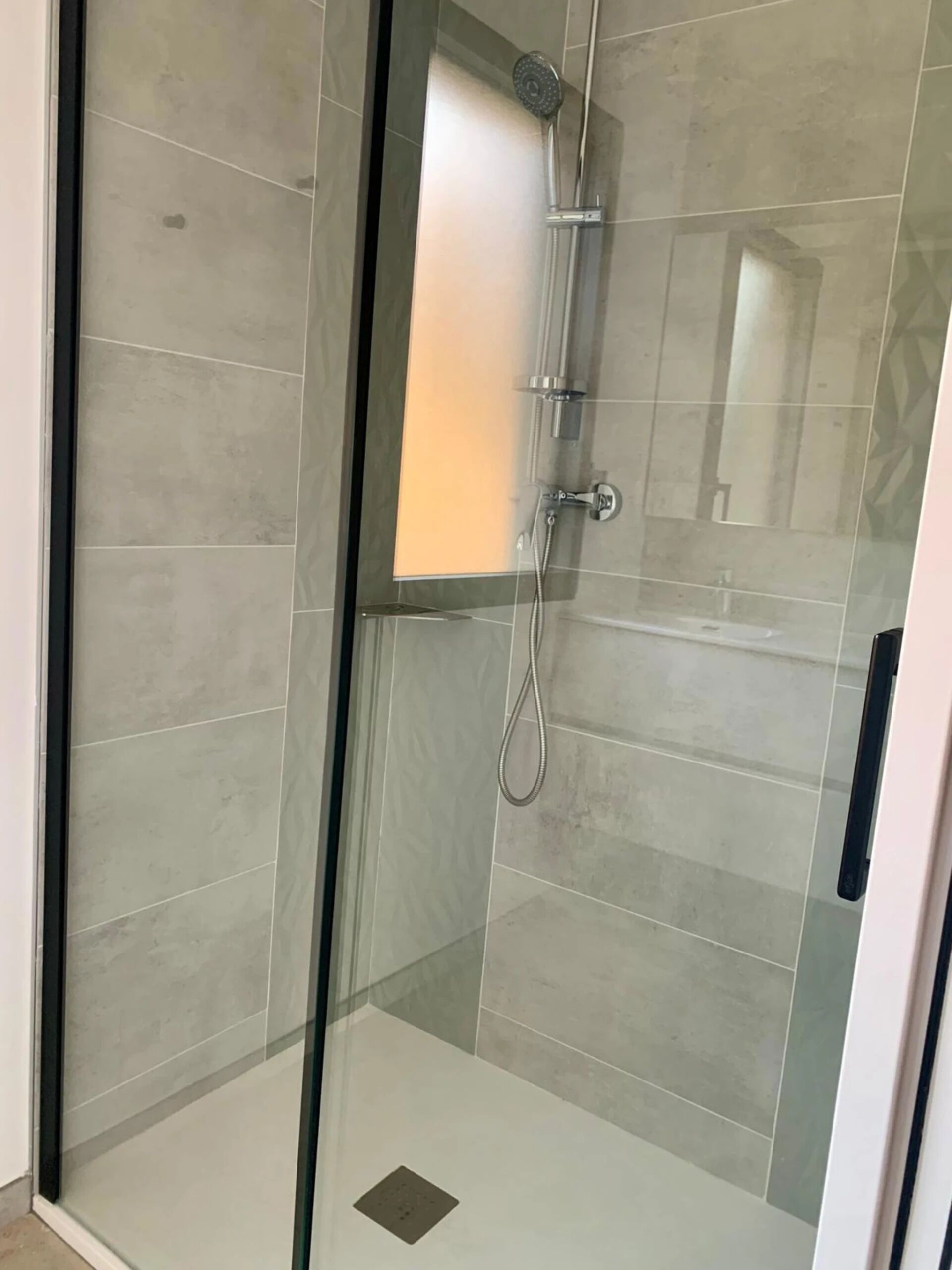 A glass-enclosed shower with a handheld showerhead and a wall-mounted faucet.
