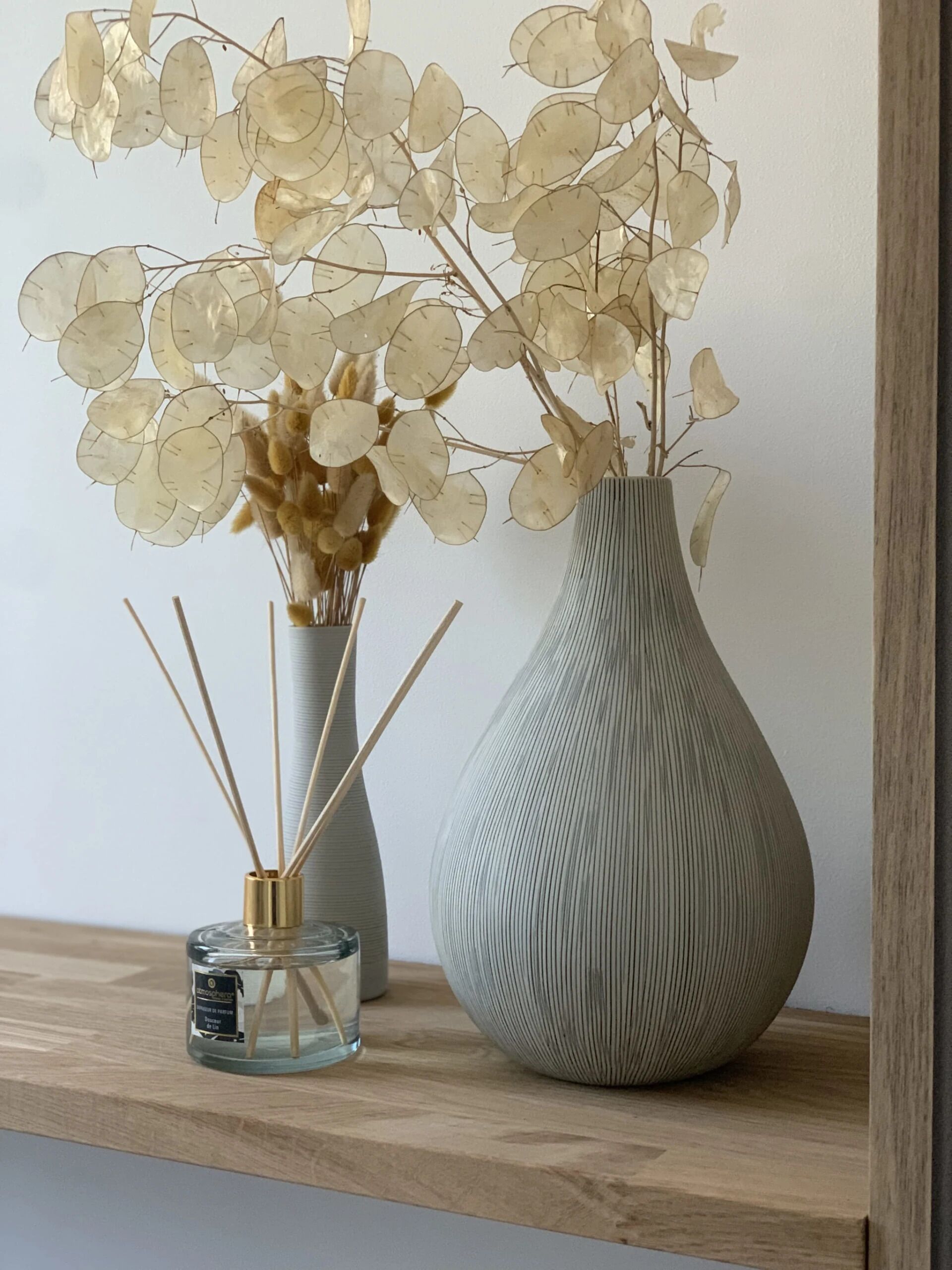 Una estantería de madera con dos jarrones que contienen flores secas y cañas.