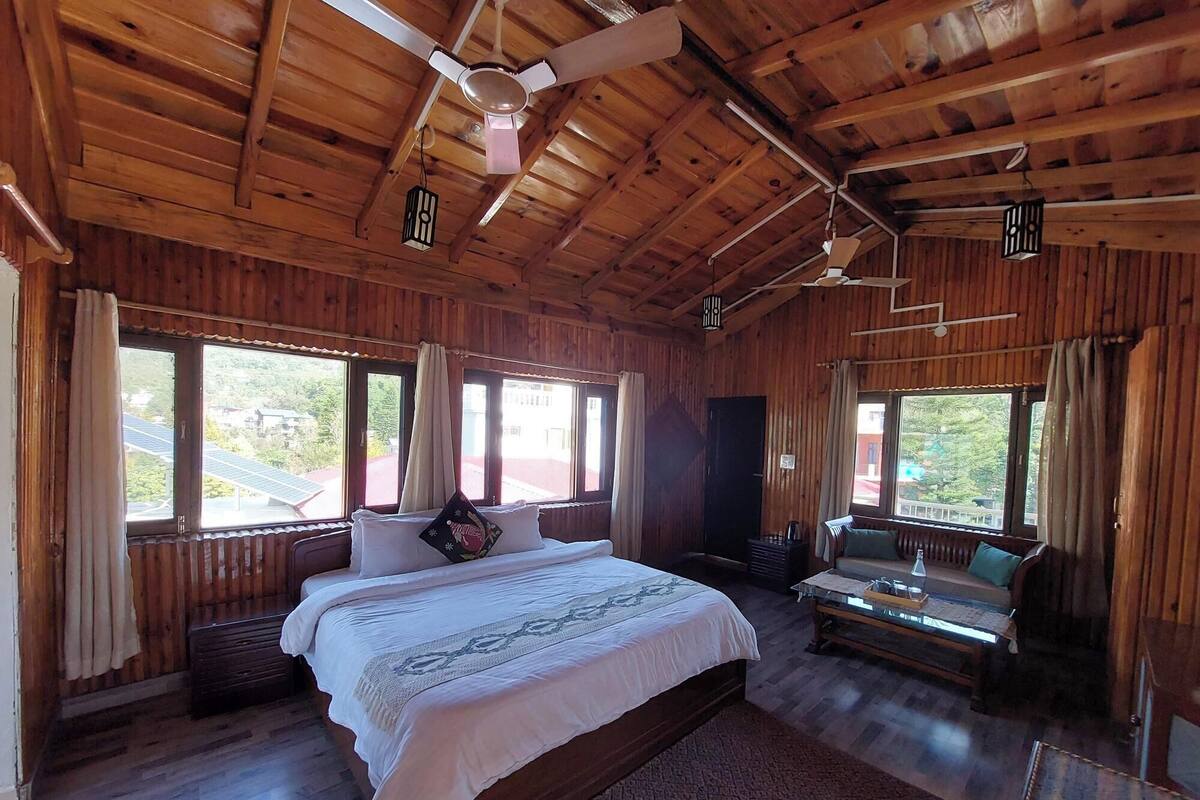 A wooden cabin bedroom with a large bed, two windows, a ceiling fan, and a small table.