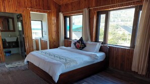 A wooden room with a large bed, a small table with drinks, and a view of greenery outside. - Alinda House Naukuchiatal by THE GHAUR (Uttarakhand)