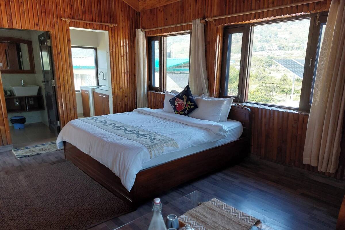 A wooden room with a large bed, a small table with drinks, and a view of greenery outside.