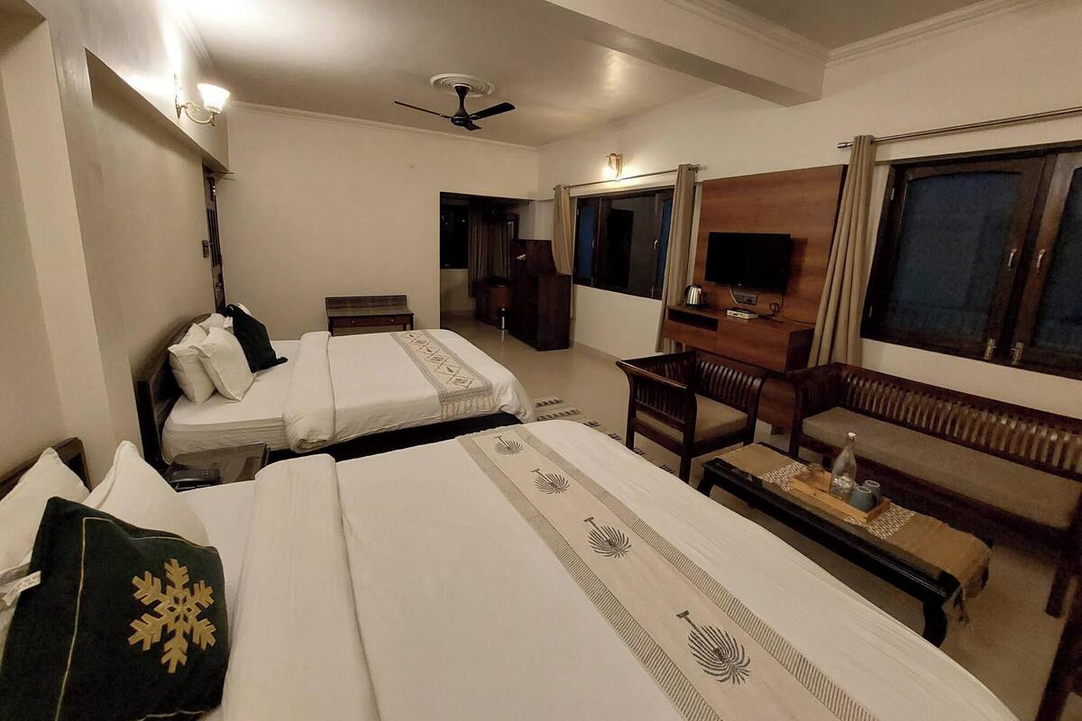 A hotel room with two beds, a sofa, a TV, and a ceiling fan.