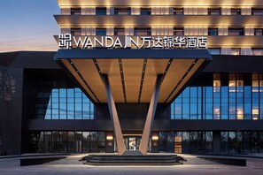 A modern hotel entrance with a prominent sign, large glass windows, and a geometric canopy structure. - Wanda Jin Ordos (Ordos)