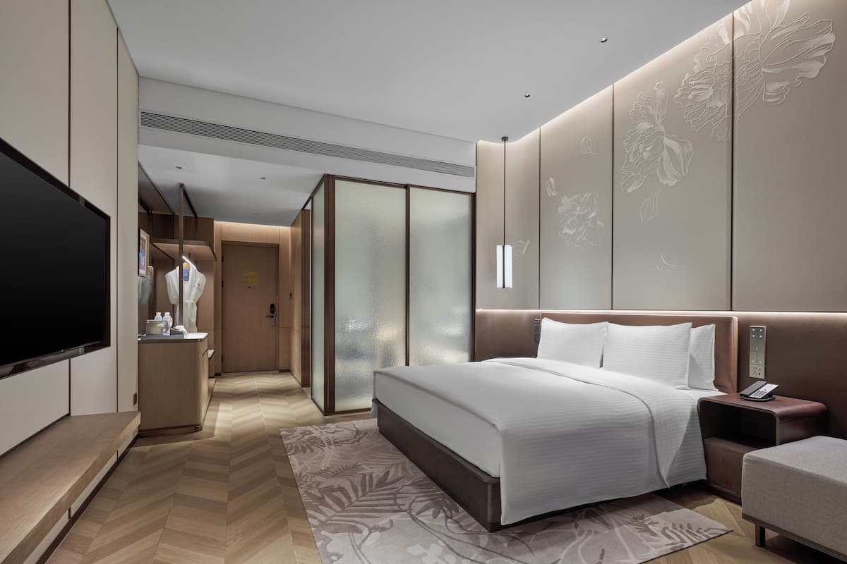 A modern hotel room with a large bed, a flat-screen TV, a bedside table, and a nightstand.