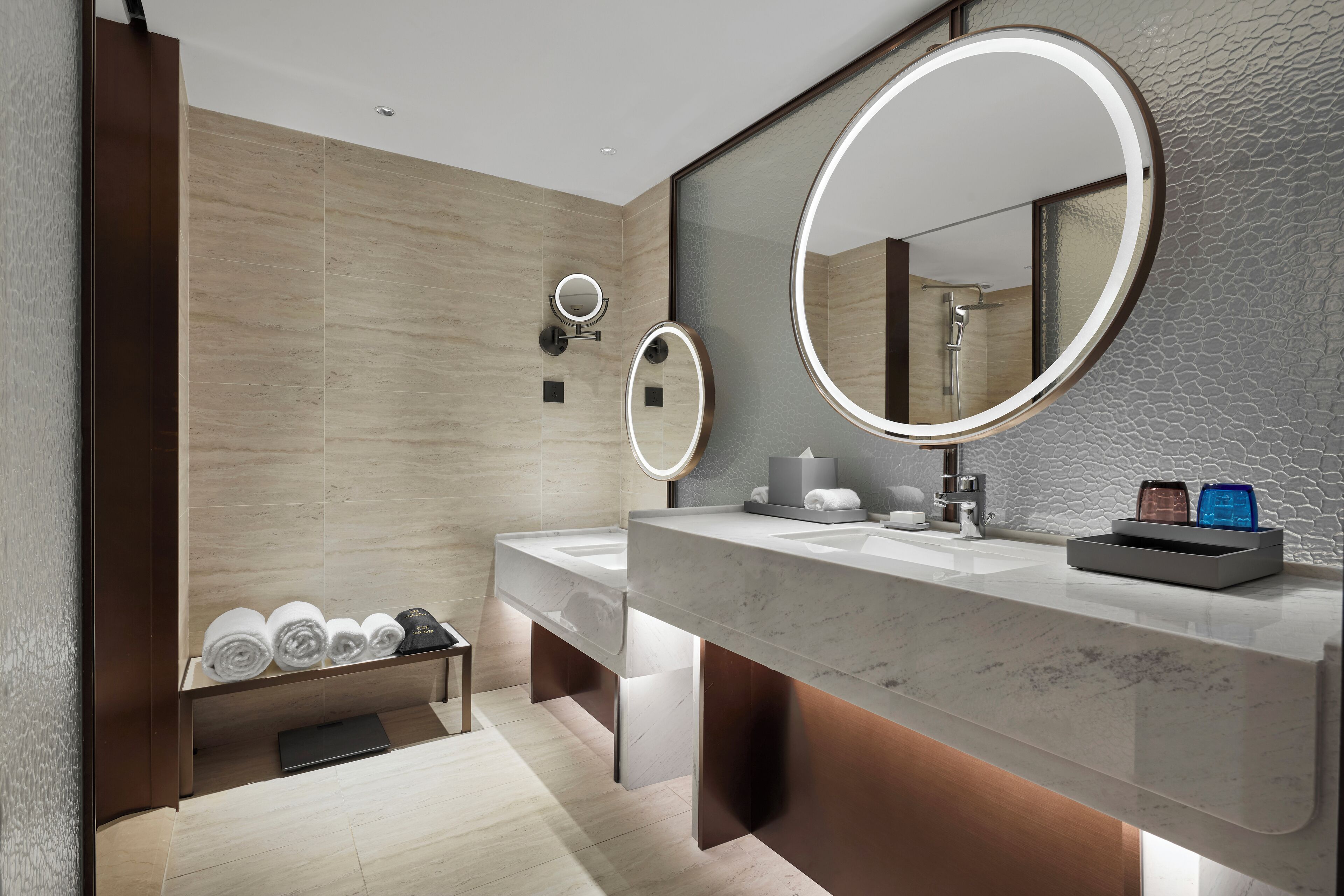 A modern bathroom with two sinks, a large mirror, and a towel rack with neatly rolled towels.