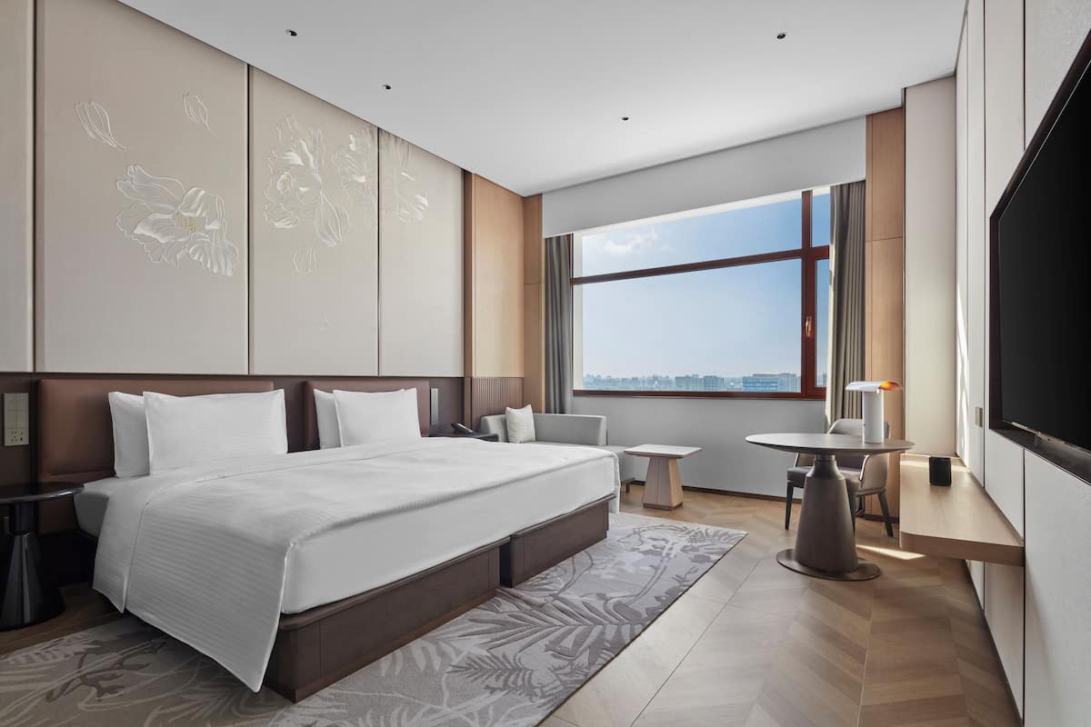 A modern hotel room with a large bed, a dining area, and a TV.