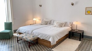 Une chambre avec deux lits, une chaise, un banc, une table de chevet avec une lampe et un sol à motifs.