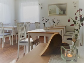 Ein Essbereich mit weißen Stühlen, einem Holztisch und einer Blumenvase.