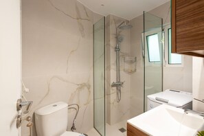 A modern bathroom with a glass-enclosed shower, a toilet, and a washing machine. - Renovated 2-bedroom Apt Near the Athenian Coast (Palaio Faliro)