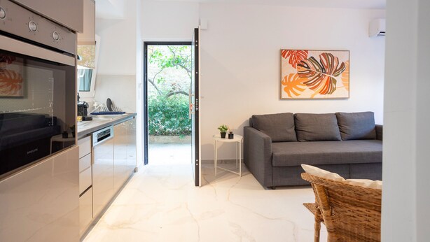A modern kitchen with a built-in oven and microwave, a grey sofa, and a wicker chair. - Renovated 2-bedroom Apt Near the Athenian Coast (Palaio Faliro)