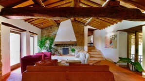 Un vaste espace de vie agrémenté d’une cheminée en pierre, de meubles rouges et blancs et d’un plafond en bois.