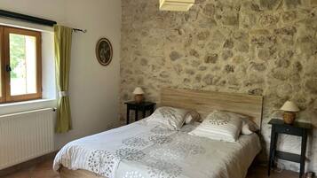 Una camera da letto con parete in pietra, un letto di legno, due comodini con lampade e una finestra con tende.