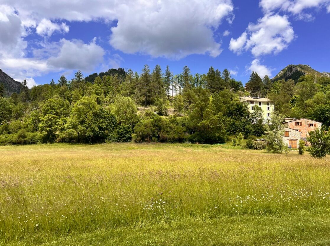 A rural landscape with a field in the foreground and a building with a sloped roof in the background.