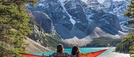 A hammock between two people overlooking a turquoise lake with mountains in the background.