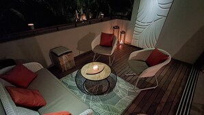 Ein gemütlicher Sitzbereich im Freien mit Korbmöbeln, Kissen und einem Tisch mit Kerze in der Mitte.