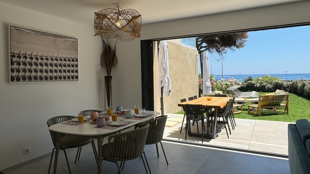 Comedor con una mesa preparada para cuatro, un ventanal con vista al mar y una lámpara decorativa en el techo.