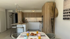 Una cocina moderna con armarios de madera, una mesa de comedor dispuesta para el desayuno y un amplio ventanal con vistas al ambiente.