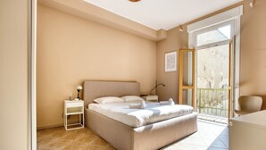 Een slaapkamer met een bed, nachtkastjes, een kleine bedlamp en een balkon met uitzicht.