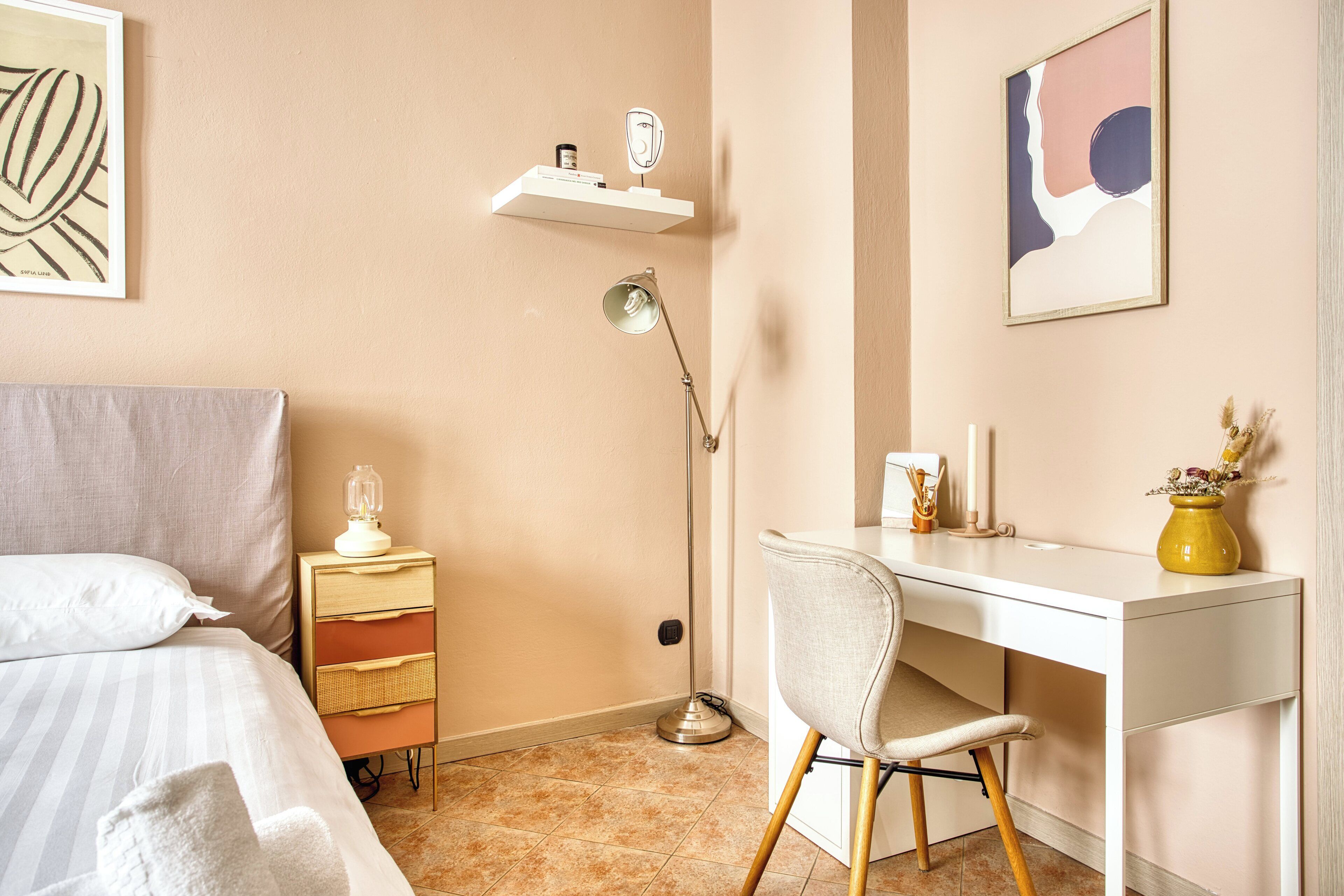 Une chambre à coucher comprenant un lit, une table de chevet avec une lampe, un bureau avec une chaise et des œuvres d’art accrochées aux murs.