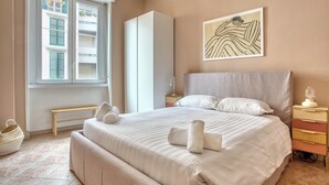 Een netjes ingerichte slaapkamer met een groot bed, een nachtkastje, een bankje en een raam met luiken.
