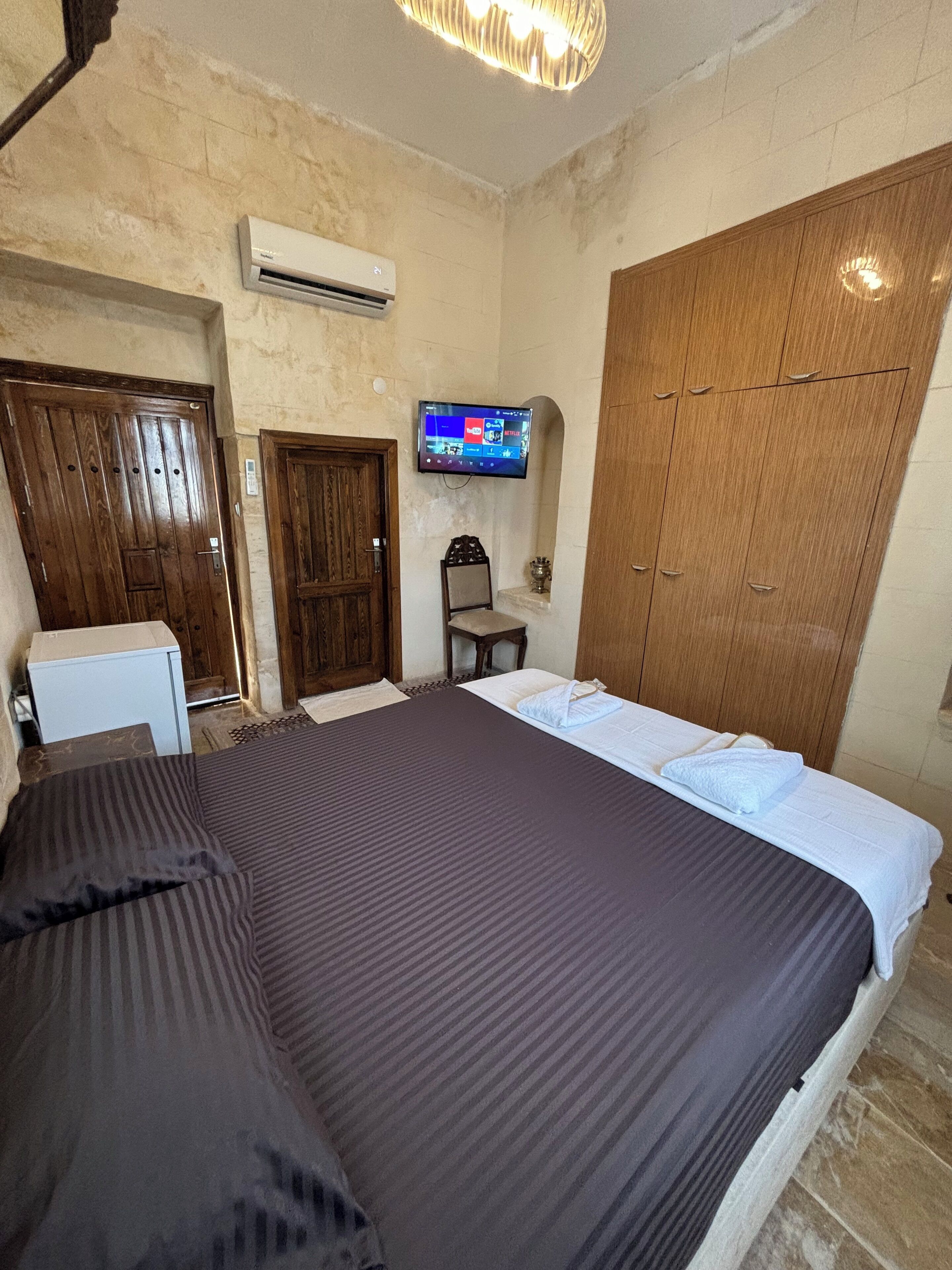 Une chambre d’hôtel comprenant un lit, un téléviseur fixé au mur, une armoire et un bureau avec une chaise.
