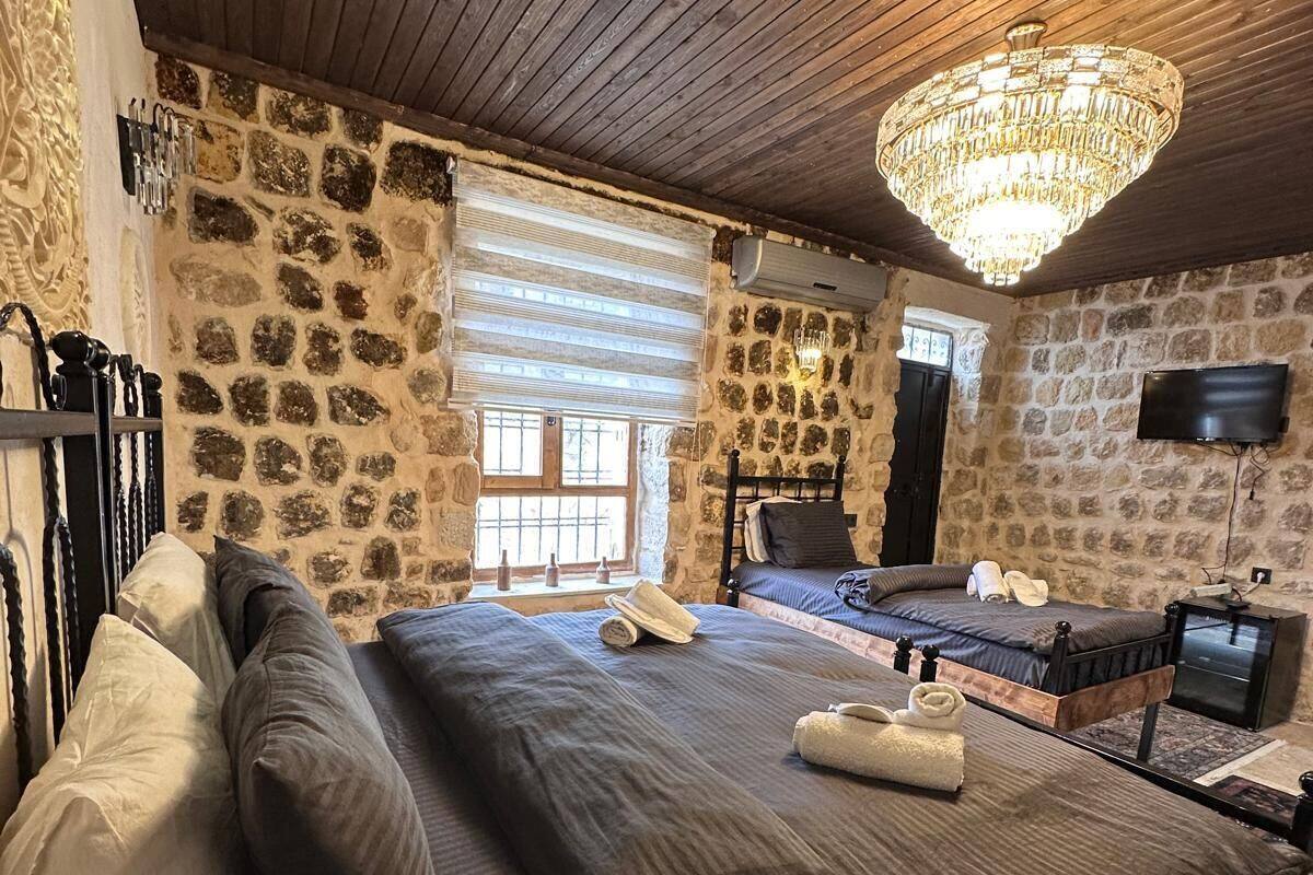Ein Schlafzimmer mit Steinsturz, Holzbalkendecke, einem großen Bett mit Kissen, einer Kandelaber und einem Fernseher an der Wand.