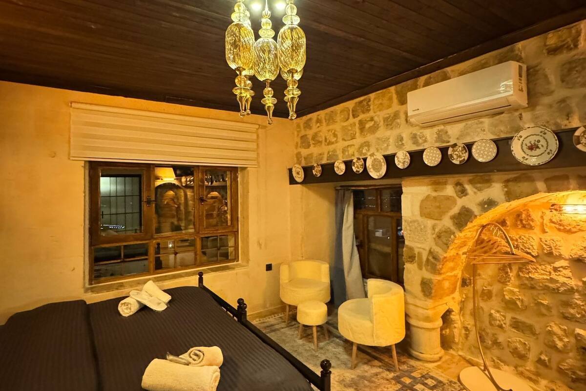 Ein gemütliches Schlafzimmer mit einem Bett, einem Kamin aus Stein, einer Chandelier und einem Fenster mit Blick.