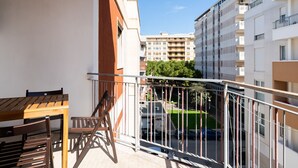 A balcony with a wooden table and chairs, overlooking a parking area and adjacent buildings.