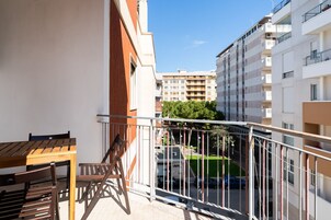 Un balcone con tavolo e sedie in legno, affacciato su un'area di parcheggio e edifici circostanti.