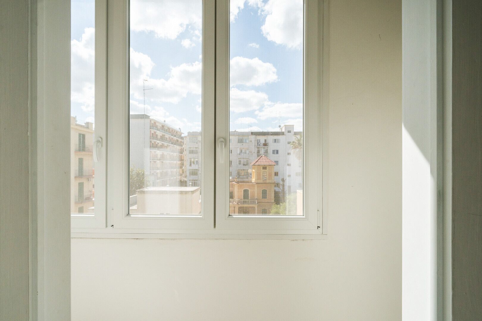 A window with a view of a building complex, including a tower-like structure.