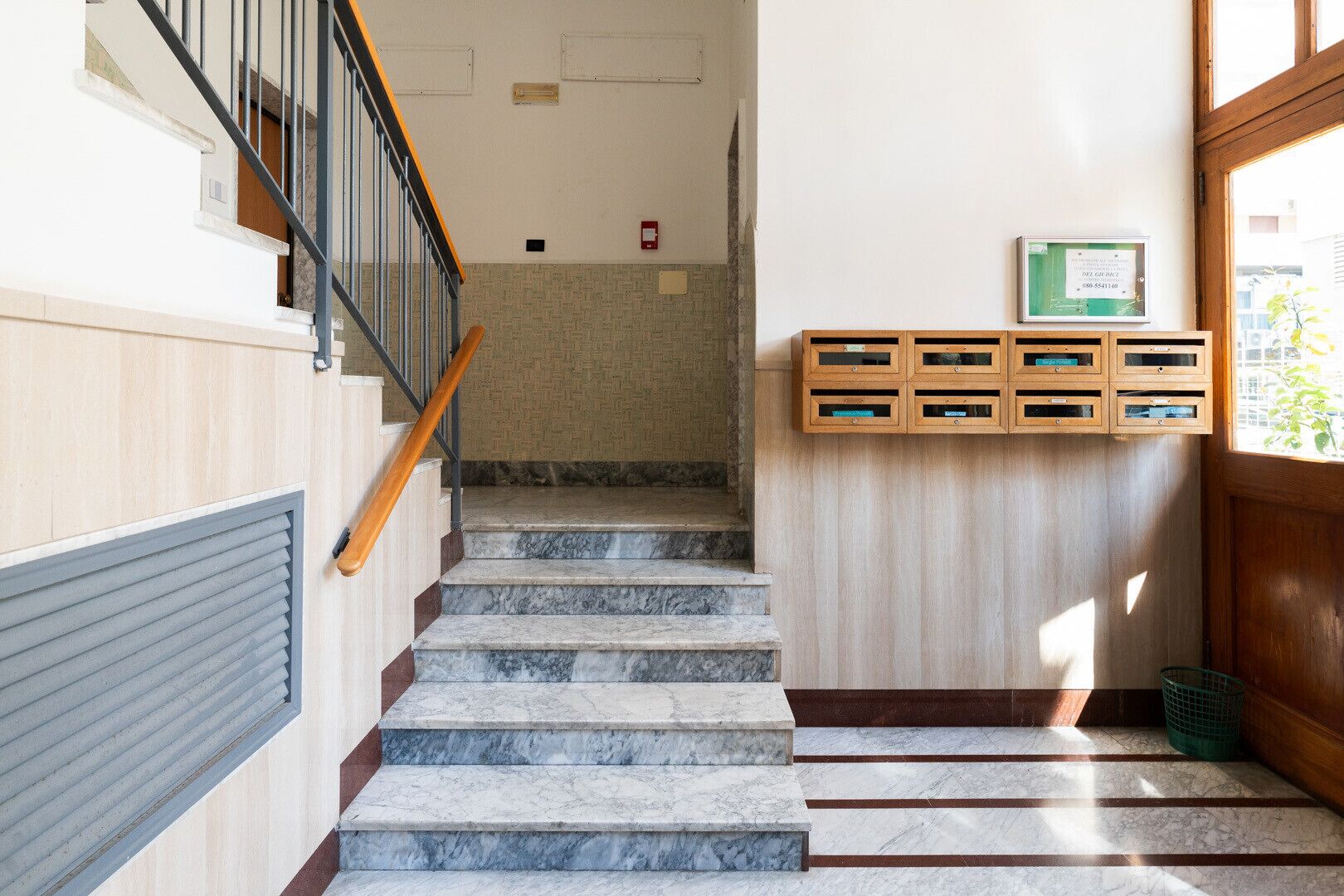 A staircase with marble steps, wooden handrails, and a wall-mounted mailbox.