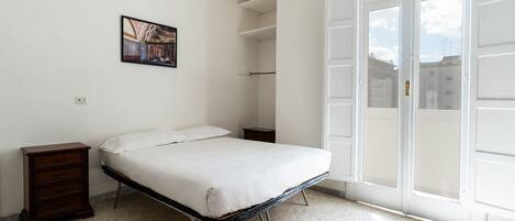 Un dormitorio con cama, cómoda, un cuadro y un amplio ventanal con vistas a edificios.