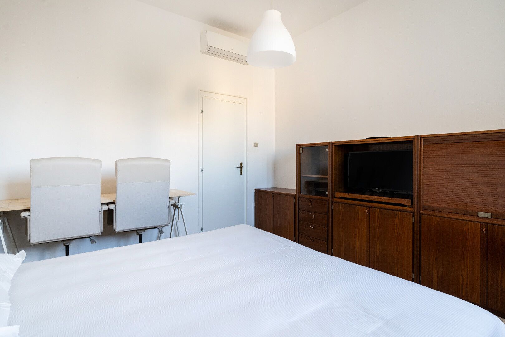 A hotel room with a bed, a desk with two chairs, a television, and a wardrobe.