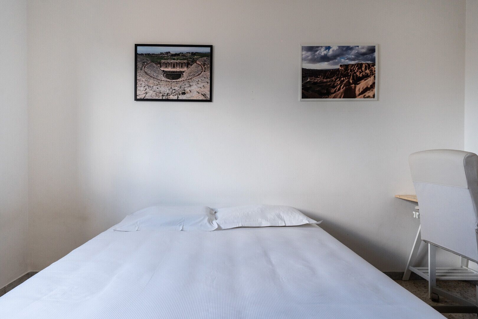 Ein Hotelzimmer mit einem Bett, einem Sessel und zwei gerahmten Bildern an der Wand.