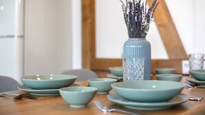 Une table à manger avec plusieurs bols et assiettes, un vase de lavande et une chaise en bois.
