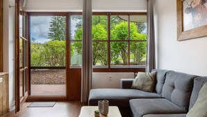 Une pièce avec un canapé gris, une petite table ornée de deux vases et une vue sur la verdure grâce à de grandes fenêtres.
