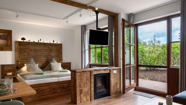 Une chambre moderne avec une tête de lit en bois, un téléviseur à écran plat, une cheminée et une grande fenêtre donnant sur un paysage verdoyant.