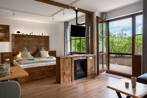Een moderne slaapkamer met een houten hoofdeinde, een flatscreen televisie, een open haard en een groot raam met uitzicht op groen.