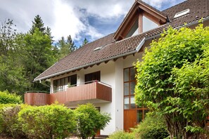 Een twee verdiepingen tellend huis met een balkon, omgeven door groen.