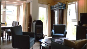 A living room with a fireplace, two armchairs, a television, and a dining area with a table and chairs. - Holiday Home 'Strandpark Baabe' with Private Terrace and Wi-Fi (Baabe)