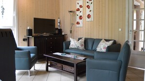 A living room with a sofa, armchairs, a coffee table, a TV, and decorative wall art. - Holiday Home 'Strandpark Baabe' with Private Terrace and Wi-Fi (Baabe)
