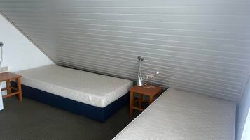 Een kleine kamer met enkel een bed, een nachtkastje en een lamp, met een schuine wand.