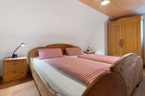 A bedroom with a wooden bed, two bedside tables with lamps, a wooden wardrobe, and a checkered bedspread.