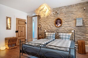 Une chambre avec un mur en pierre, un lit avec une literie à carreaux, une tête de lit en bois et un luminaire suspendu.